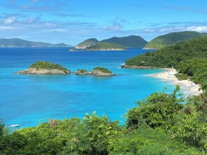 A coastal landscape with clear blue waters, a sandy beach, and lush greenery.