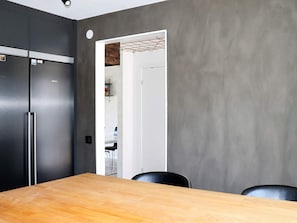 Una cocina moderna con un refrigerador negro, una mesa de comedor de madera y una pared gris.