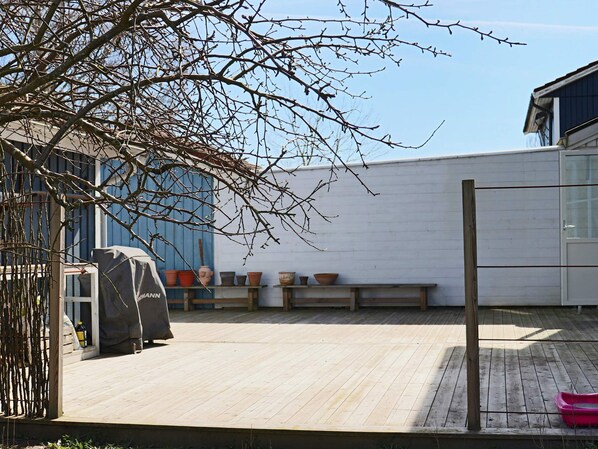 Una terraza de madera con un banco, plantas en macetas y una zona cubierta para la parrilla.