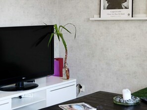 A flat-screen TV on a white stand, a potted plant, a framed photo, and a candle on a table. - 4 Star Holiday Home in Halmstad (Halmstad)