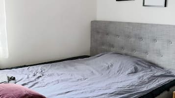 Una cama individual con cabecera gris y cubrecolchón gris.