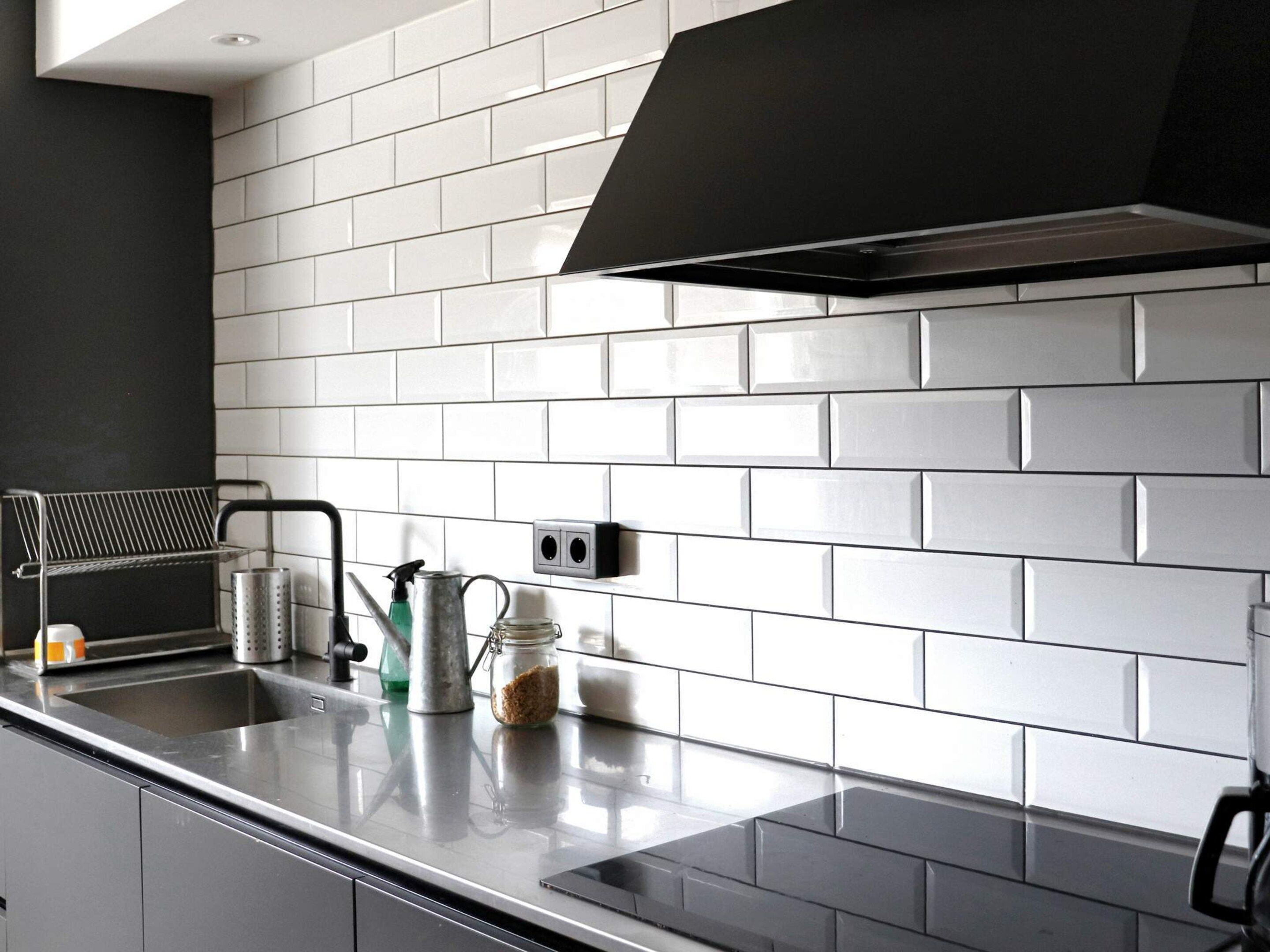 A kitchen with white subway tiles, a black range hood, and stainless steel appliances.