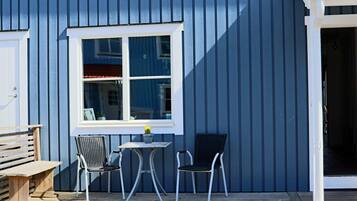A blue building with a white window, two chairs, a small table, and a bench outside.