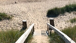 Una playa arenosa con un camino de madera que lleva al agua.
