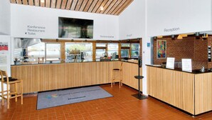 Ein Empfangsbereich mit Holztresen, einer Rezeption und Hinweisschildern für Konferenzrestaurant und Toilette.