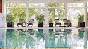 Ein überdachter Swimmingpool mit klaren Glaswänden, umgeben von Topfpflanzen und Korbstühlen.
