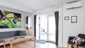 A modern living room with a sofa, a coffee table, and a chair. There is a large abstract painting on the wall, a door leading outside, and an air conditioning unit on the wall. - 8 Person Holiday Home on a Holiday Park in Karrebaeksminde (Karrebæksminde)