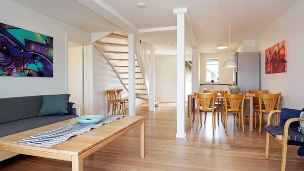 A modern living room with a sofa, dining table, and chairs. A staircase leads to an upper level. - 8 Person Holiday Home on a Holiday Park in Karrebaeksminde (Karrebæksminde)