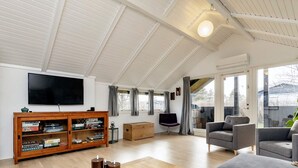 Amplia sala de estar con techo alto, televisor montado en la pared, mueble de entretenimiento de madera con juegos de mesa y un ventanal con vistas al exterior.