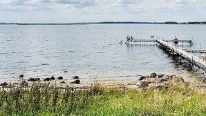 Een rustig meer met een steiger die het water in reikt, omringd door rotsen en begroeiing.