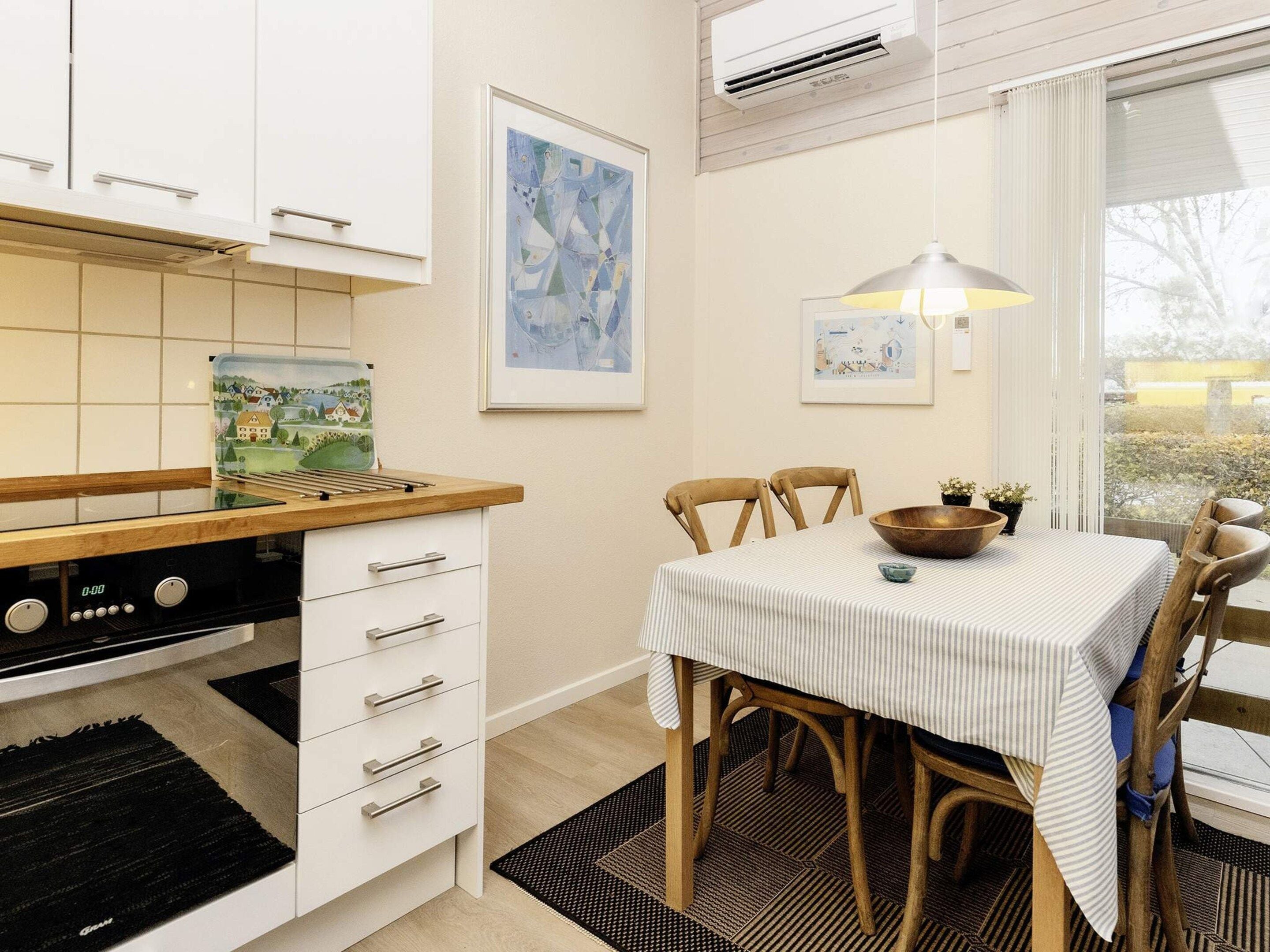 A kitchen with a stove, white cabinets, a dining table with chairs, and artwork on the wall.