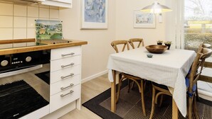 A kitchen with a stove, white cabinets, a dining table with chairs, and artwork on the wall. - 4 Person Holiday Home in Aeroskobing (Aeroskobing)