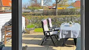 Une terrasse extérieure avec une table et des chaises, un barbecue et une plante en pot.