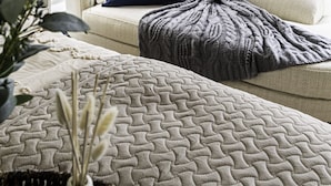 Una habitación acogedora con un sofá color beige, una almohada azul y una manta estampada.