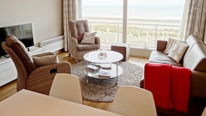 A living room with a large window, a television, a sofa, a chair, and a coffee table. - Apartment in Nieuwpoort With sea View (Nieuwpoort)