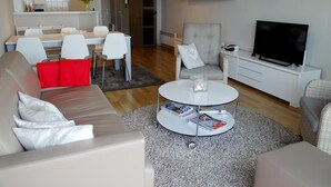 A modern living room with a sofa, armchair, coffee table, and a TV. - Apartment in Nieuwpoort With sea View (Nieuwpoort)