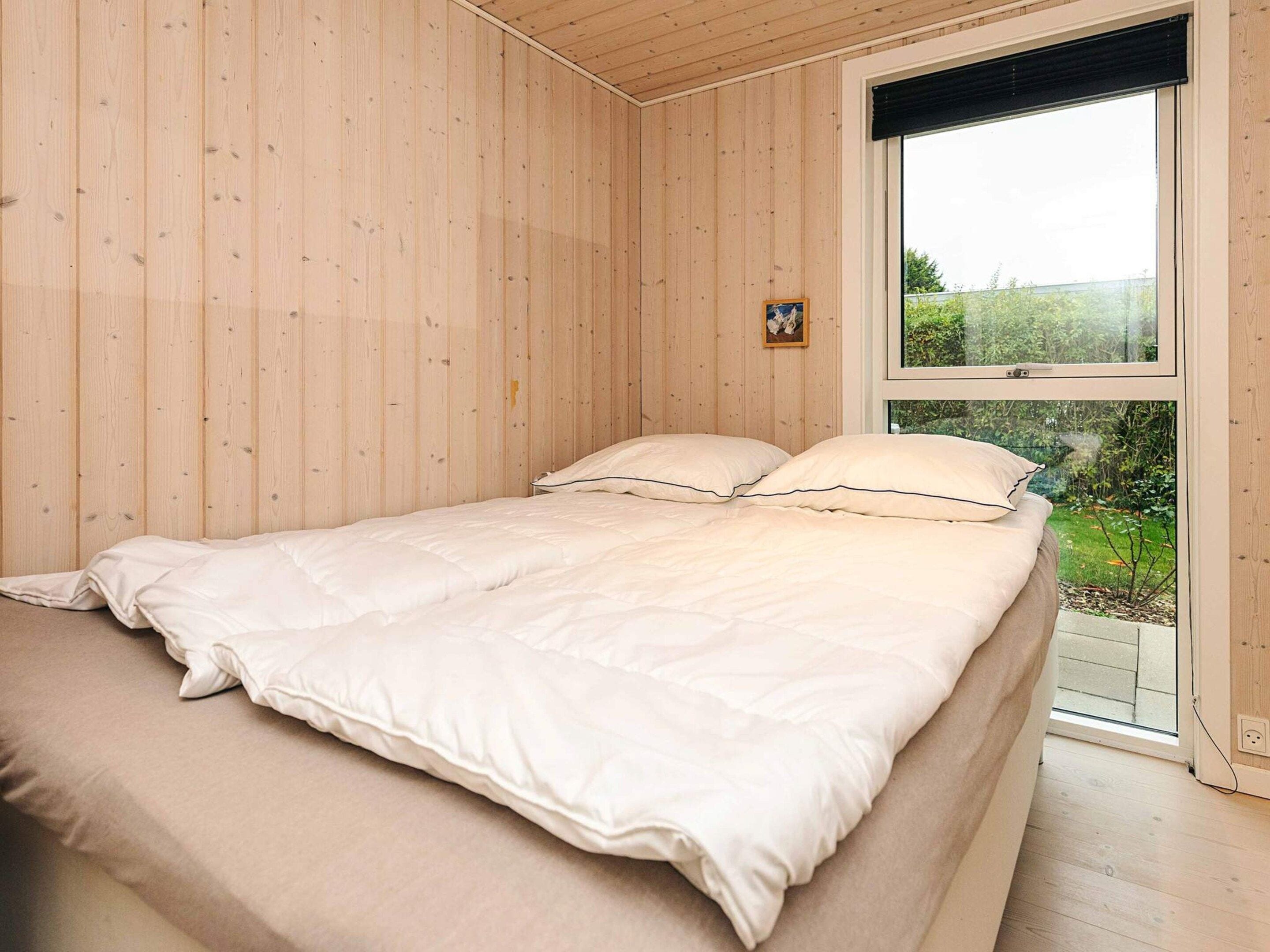 Een slaapkamer met een bed, houten wanden, een raam en een klein schilderij.