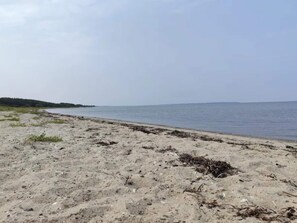 En sandstrand med rolige bølger, en fjerntliggende kystlinje og en klar himmel.