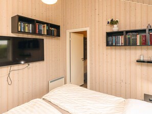 A bedroom with a bed, a TV mounted on the wall, and two bookshelves filled with books. - 8 Person Holiday Home in Bogense (Bogense)