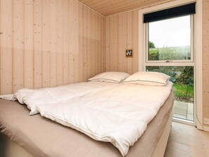 A bedroom with a wooden paneled wall, a bed with white bedding, and a window with a view of greenery. - 8 Person Holiday Home in Bogense (Bogense)