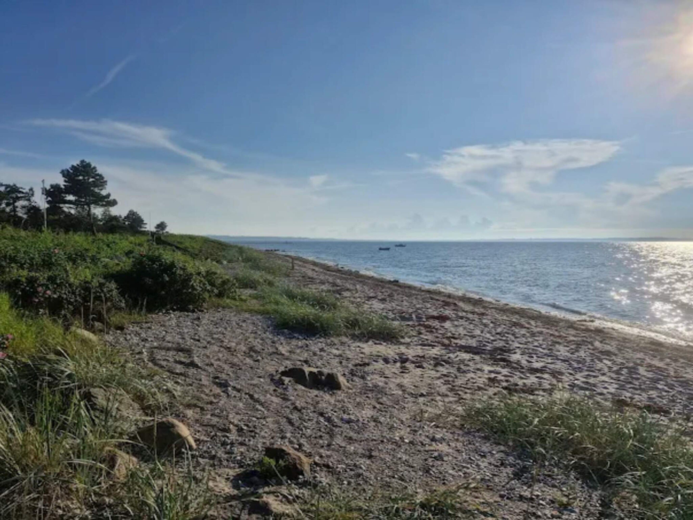 A beach with a clear sky, a sandy shore, and a few boats in the distance.