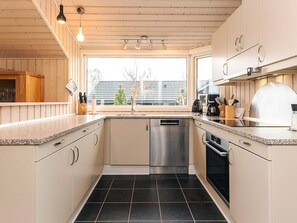 A modern kitchen with wooden cabinets, a stainless steel dishwasher, and a large window providing a view of the outside. - 8 Person Holiday Home in Bogense (Bogense)