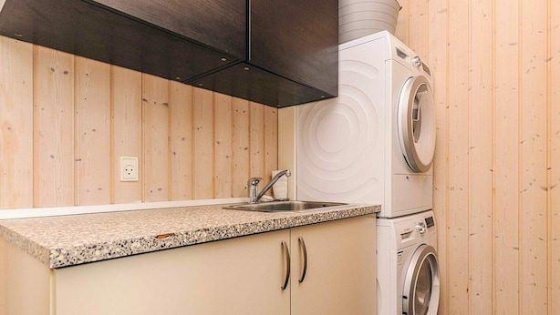 A compact kitchen with a granite countertop, a sink, and a stacked washer and dryer.