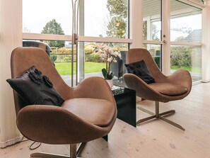 Two brown leather armchairs with black cushions, a small black table, and a view of a garden through large windows. - 8 Person Holiday Home in Bogense (Bogense)