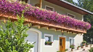 A two-story house with a balcony covered in purple flowers, a garage, and potted plants on the front porch. - Apartment in St. Stefan im Rosental (Sankt Stefan im Rosental)