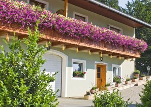 A two-story house with a balcony covered in purple flowers, a garage, and potted plants on the front porch. - Apartment in St. Stefan im Rosental (Sankt Stefan im Rosental)