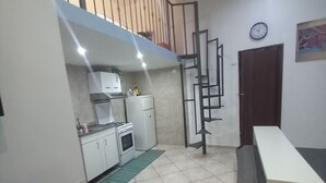 Une cuisine compacte avec un coin repas, un escalier et une horloge au mur.