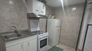 Une cuisine de taille réduite, avec des meubles blancs, une cuisinière à gaz, un évier et un petit réfrigérateur.