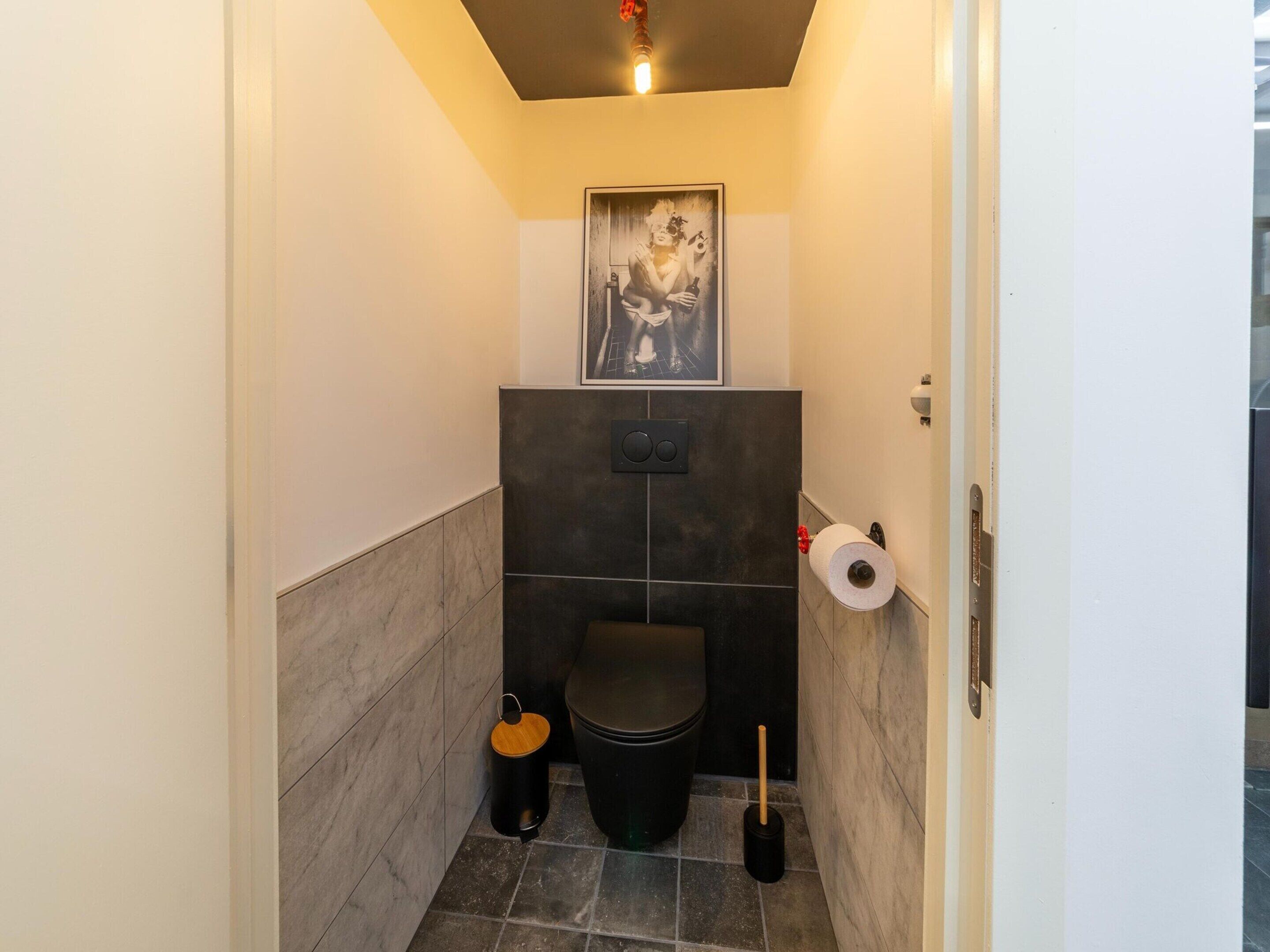 A compact bathroom with a toilet, a trash bin, a toilet brush, and a toilet paper holder.