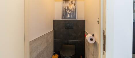 A compact bathroom with a toilet, a trash bin, a toilet brush, and a toilet paper holder.