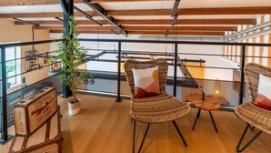 Ein geräumiger Balkon mit Korbstühlen und einem Blumentopf, mit sichtbaren Holzbalken und einem Metallgeländer.