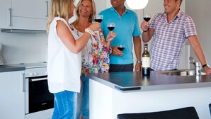 Une cuisine moderne avec des meubles blancs, un four Bosch et un îlot central sur lequel est posée une bouteille de vin.