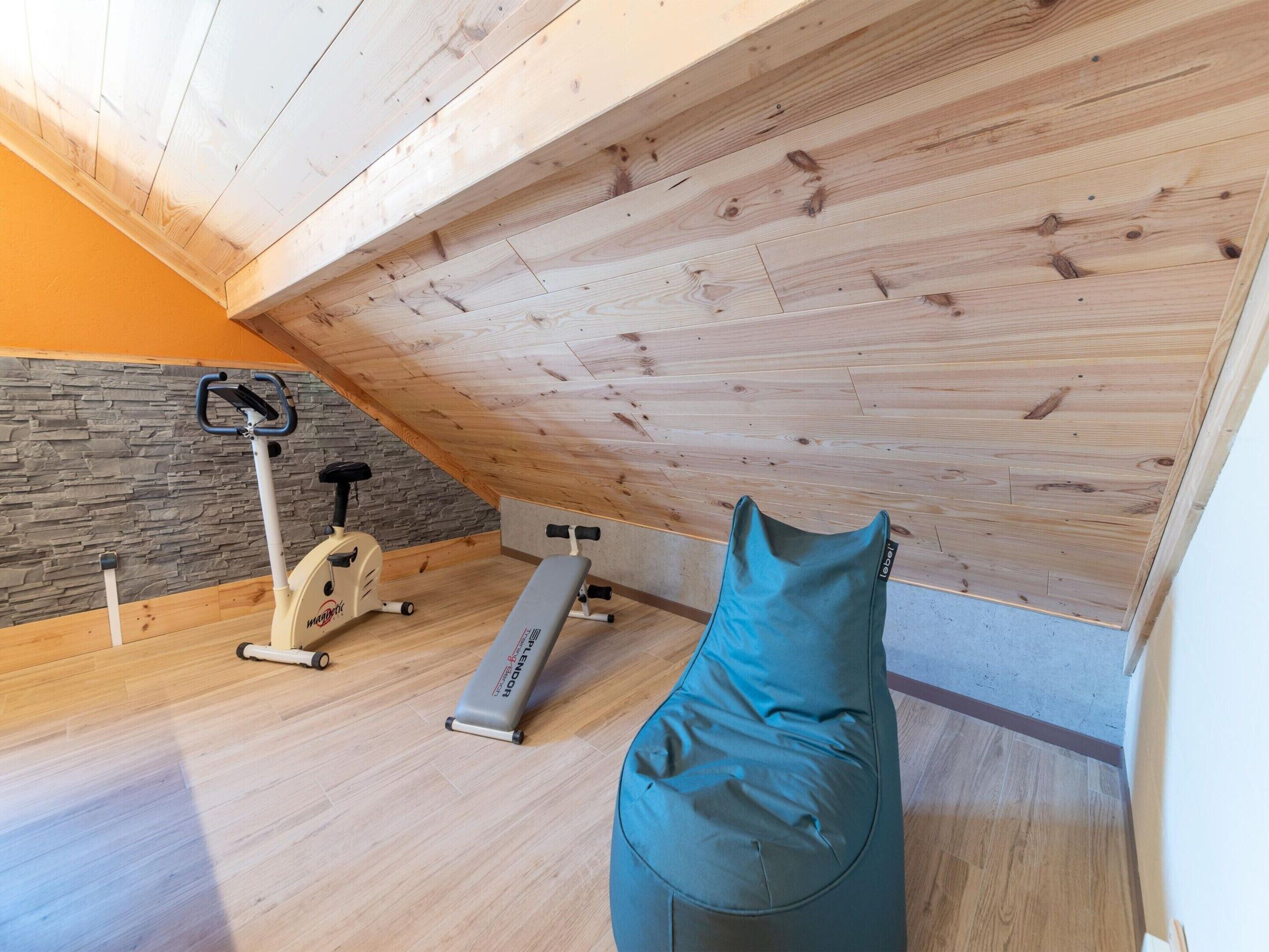 A gym with exercise equipment, a stone wall, and a sloped ceiling.