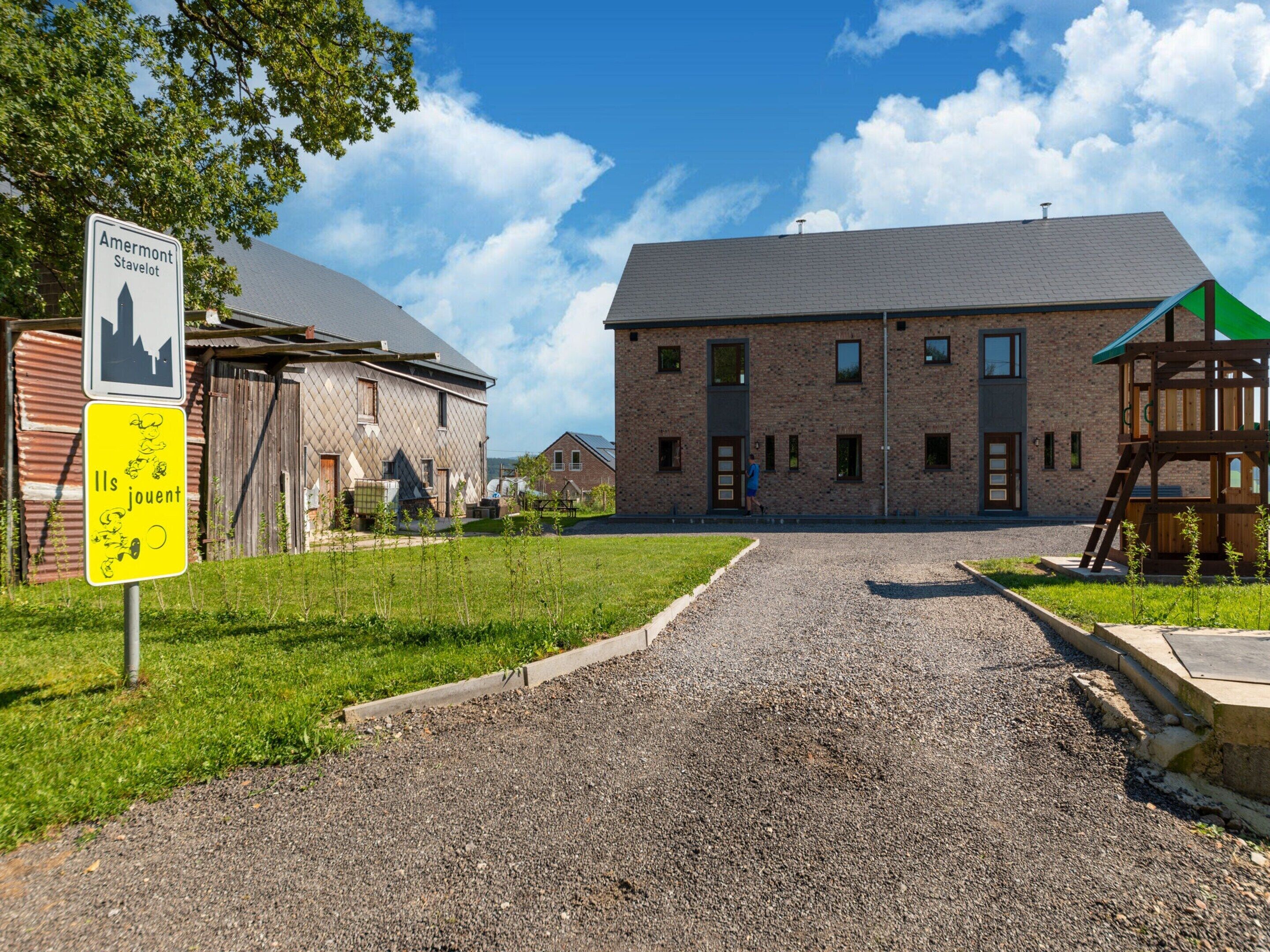 A gravel driveway leading to a brick building with a green-roofed play structure.