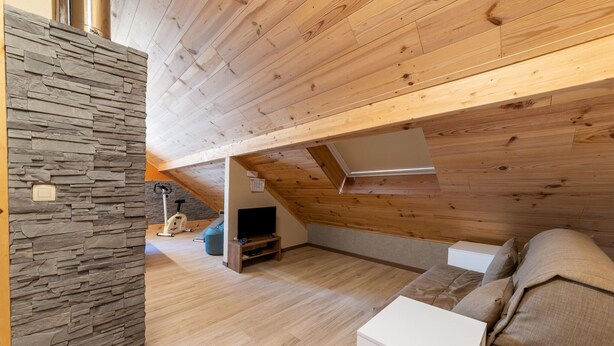 Une pièce de style loft avec un mur en pierres apparentes, des poutres en bois, une télévision, un canapé et une petite table blanche.