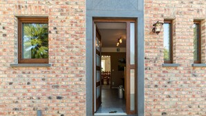 Une entrée d’immeuble avec une façade en briques, une porte en verre et une grille métallique en bas.