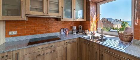 A modern kitchen with wooden cabinets, a granite countertop, and a window with a view of houses.