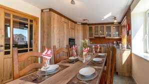 Un coin repas avec une longue table en bois, dressée pour quatre personnes, des chaises en bois et une cuisine en arrière-plan.