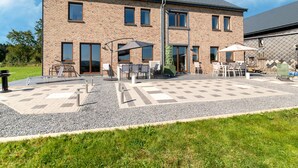 Un bâtiment à deux étages avec une façade en briques, de grandes fenêtres et un patio doté d’un espace aménagé pour s’asseoir à l’extérieur.