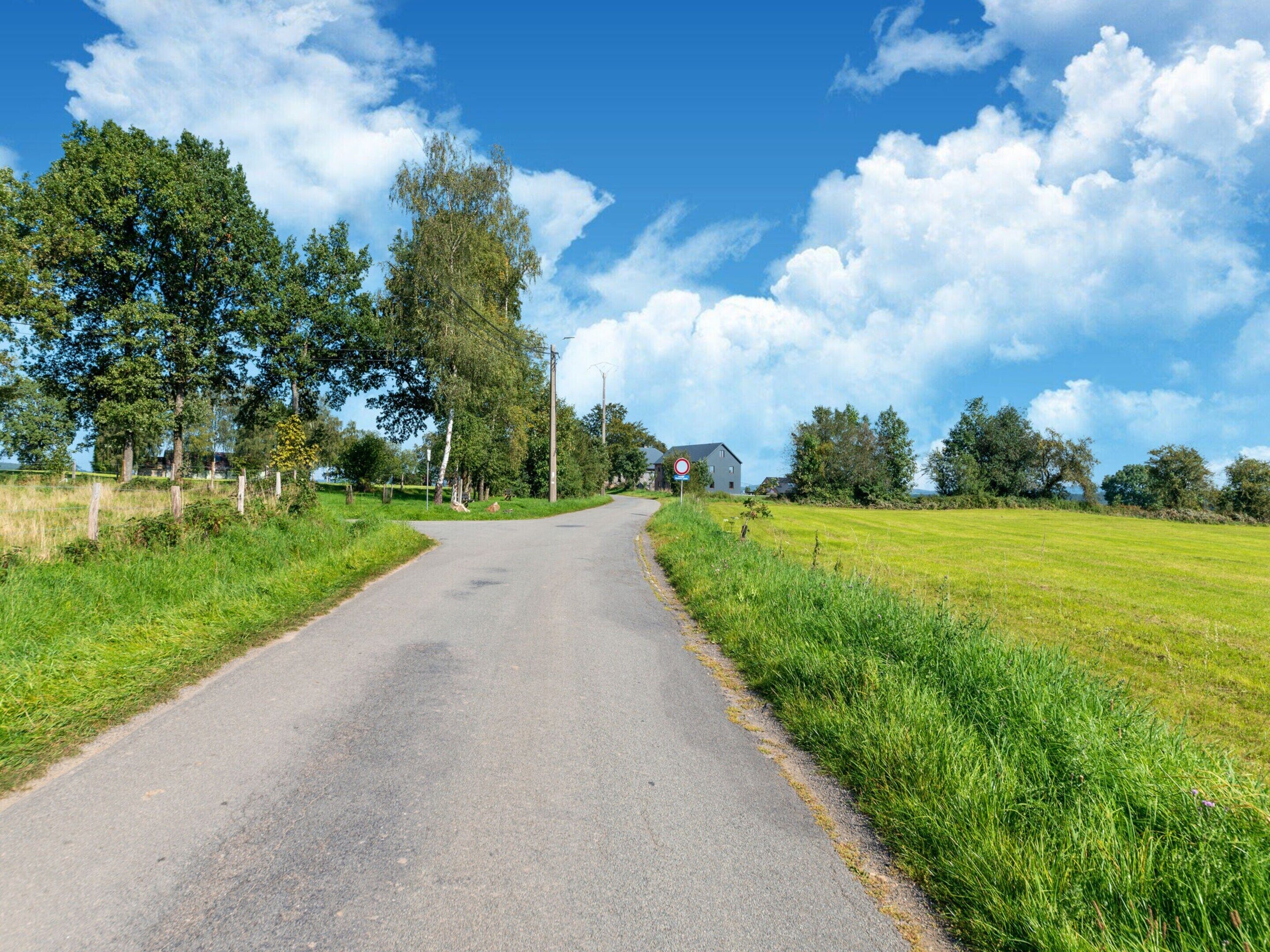 Una strada di campagna con una casa all'orizzonte, immersa tra campi e alberi.