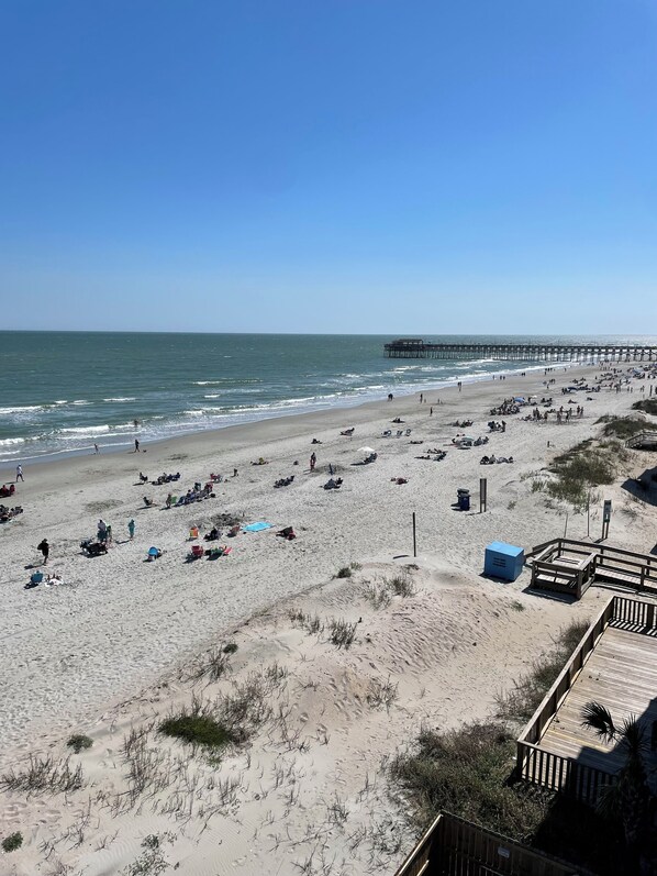 A beach with a pier extending into the ocean, sandy terrain, and a few beachgoers.