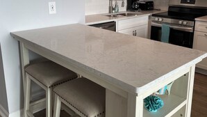 Una cocina moderna con armarios blancos, encimera de mármol e iluminación colgante.