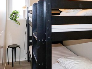 A bunk bed with a small stool beside it, a window with a plant, and a white wall. - 4 Person Holiday Home in Falkenberg (Falkenberg)