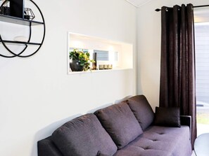 A modern living room with a dark grey sofa, a black metal shelf, and a framed picture of a kitchen. - 4 Person Holiday Home in Falkenberg (Falkenberg)