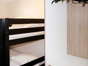 A bunk bed with white bedding and a wooden wardrobe with a light wood finish.