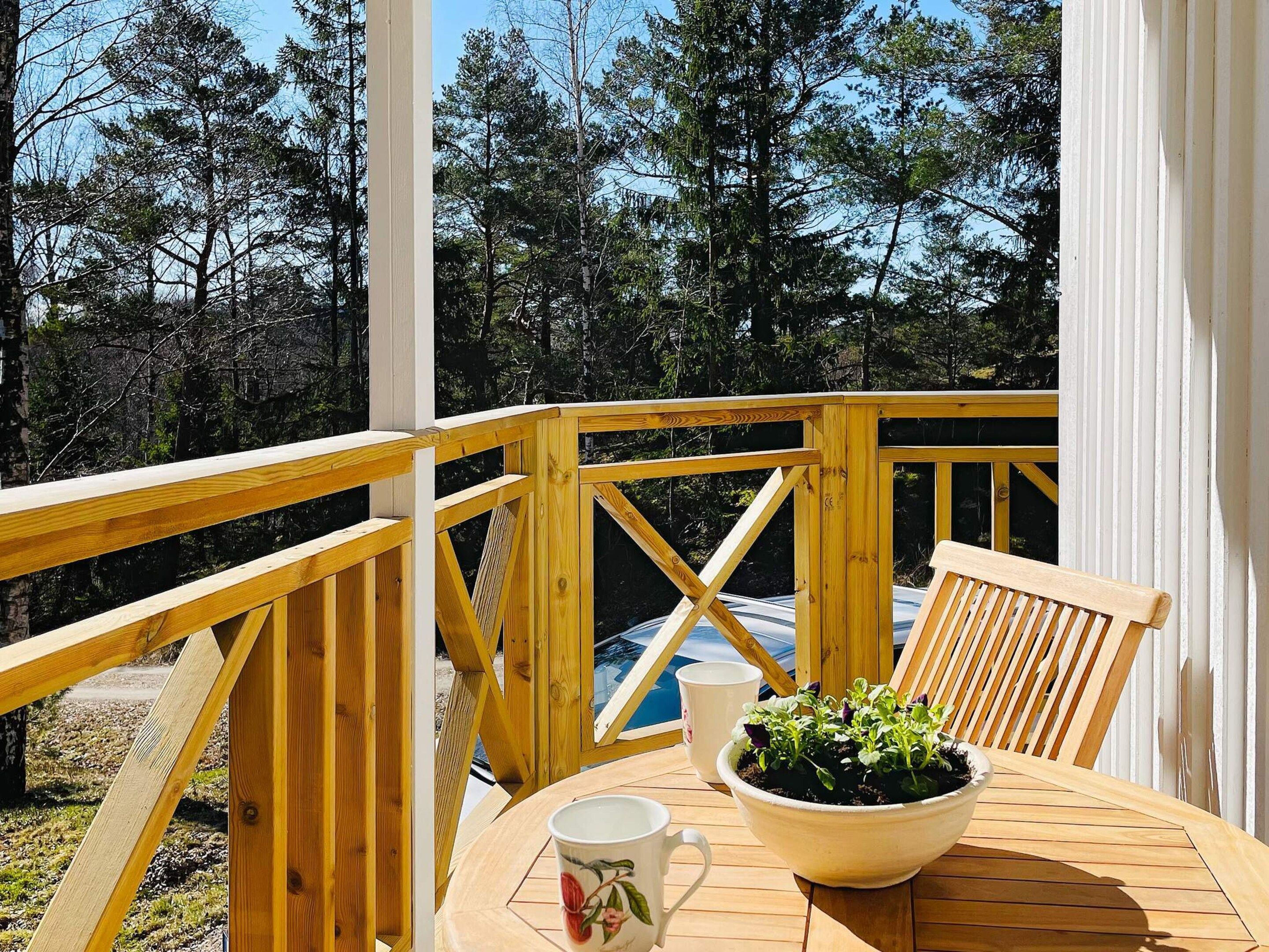 A wooden deck with a table and chairs, a potted plant, and a white mug.